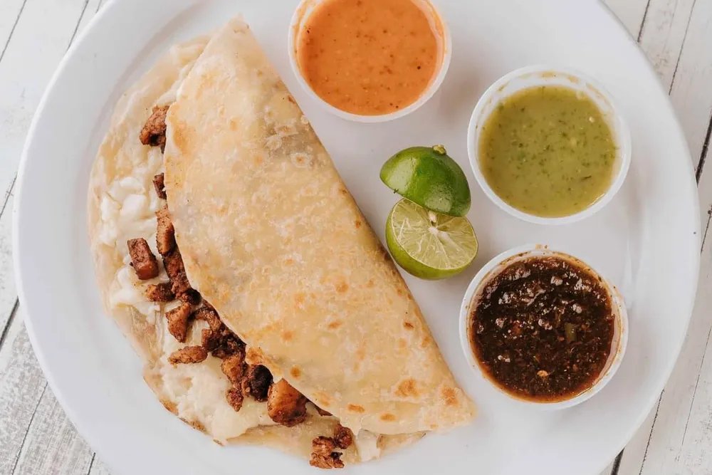 Quesadilla de harina con queso y carne asada, con salsas y limón